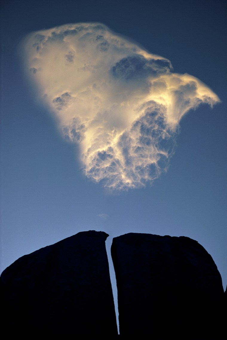 Split Rock and Cloud, Eastern Sierra, California, 1976  Galen Rowell. .Galen Rowell (1940-2002) was a master of incorporating fleeting qualities of natural light in compelling compositions. He saw this splendidly illuminated cirrus cloud floating quickly on the wind while climbing one evening in the Buttermilk region of California's Eastern Sierra Nevada. Rather than simply capturing an image of the cloud out of context with the place, Galen wished to incorporate a sense of the boulder-strewn granite landscape around him. He imagined a composition that paired the cloud with a strongly graphic silhouette, and traversed the rugged landscape to find a foreground subject in a suitable position to photograph against the sky while the cloud passed overhead. He waited only thirty seconds after setting up his tripod-mounted Nikon before the cloud floated through the perfect position.