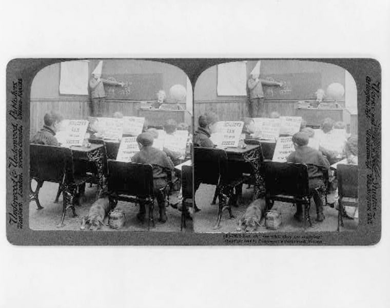 Underwood & Underwood.,  photographic print on stereo card : stereograph. Classroom with children reading various crime stories and boy, wearing dunce cap, at blackboard.