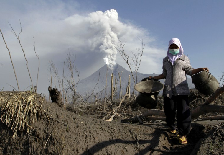 Image: Mount Merapi volcano spews ash as a villager collects her valuables from the ruins of her house at Kali Tengah village in Sleman