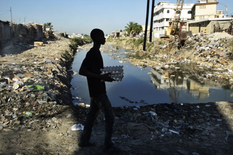 Image: A resident carries eggs while he walks past a refuse-clogged canal in downtown Port-au-Prince