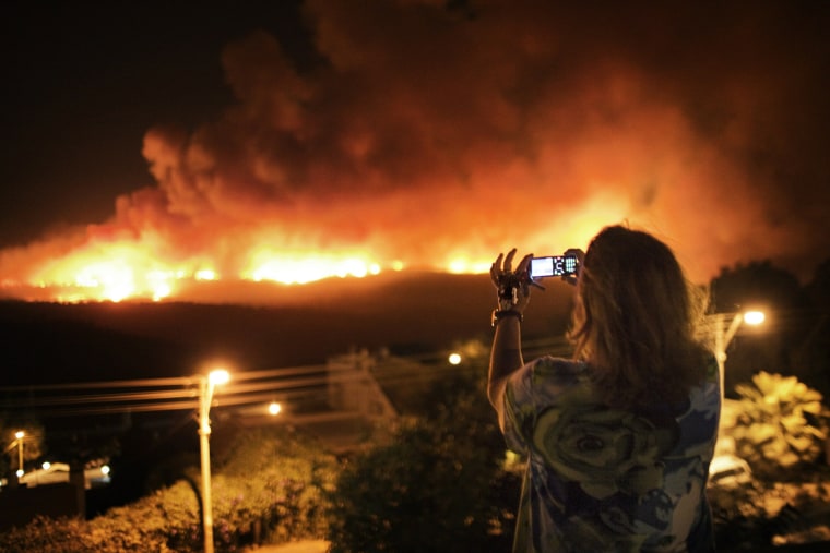 Image: An Israeli woman holds the keys of her house in her left hand while taking a photo of a raging forest fire in the Carmel mountain
