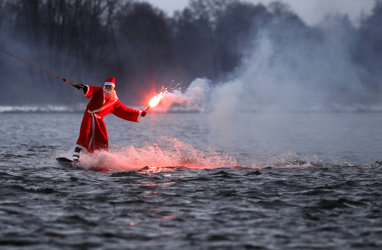 Image: A man dressed as Santa Claus holds a flare as he wakeboards in Hamburg