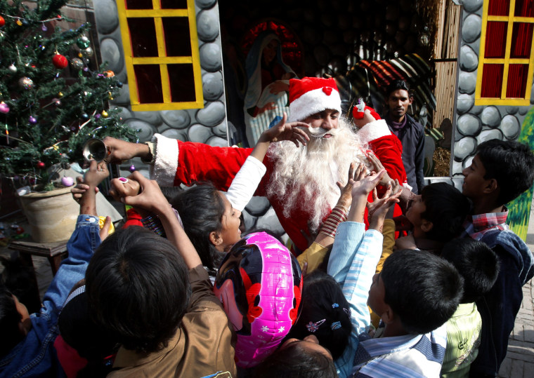 Image: A man dressed as Santa Claus distributes sweets to children at St. Anthony Church on Christmas Day in Lahore