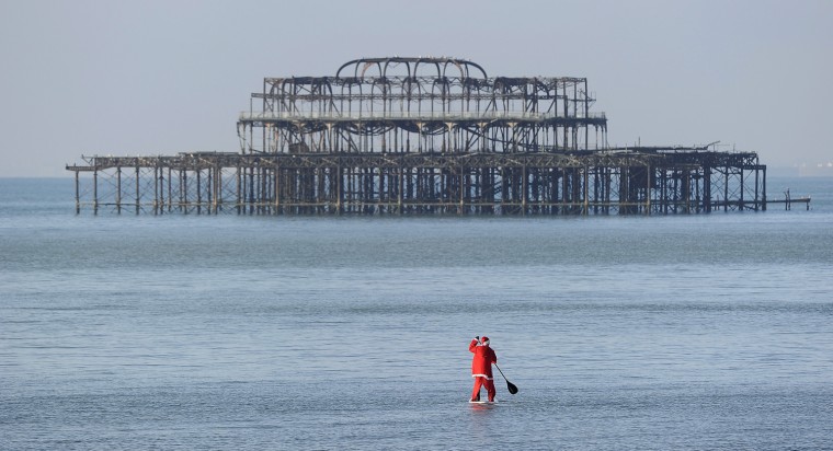 Image: A lifeguard dressed in a Santa Claus outfit paddles to sea on Brighton Beach, southern England, on Christmas Day