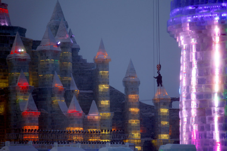 Image: Workmen hang from a crane as they put the finishing touches to an ice sculpture for the 12th Harbin Ice and Snow World display in the northern city of Harbin