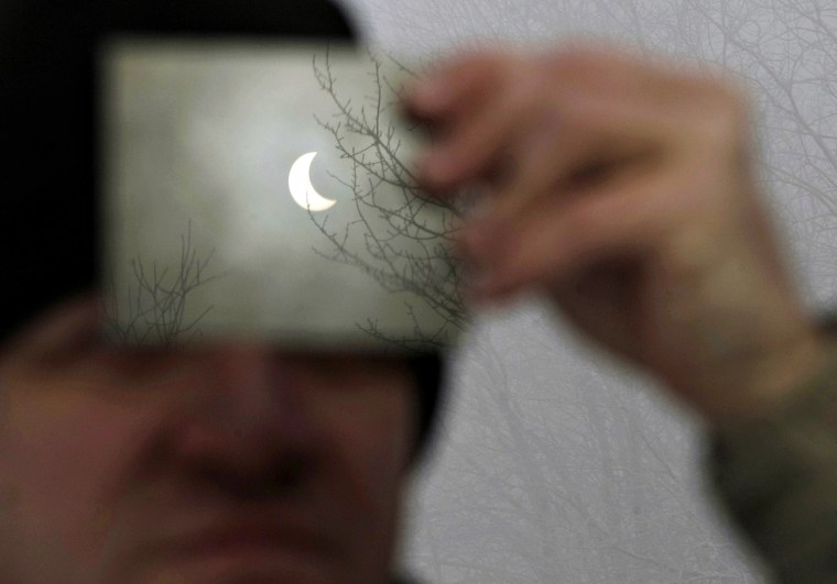 Image: A man watches a partial solar eclipse through a filter in Galyateto