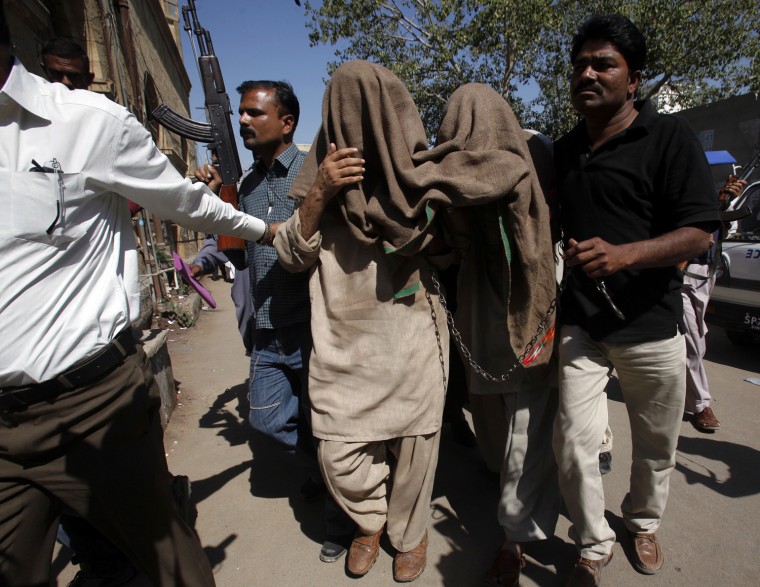 Image: Armed policemen lead two of four men, who were draped in cloth to hide their identities, after they appeared in district courthouse in Karachi