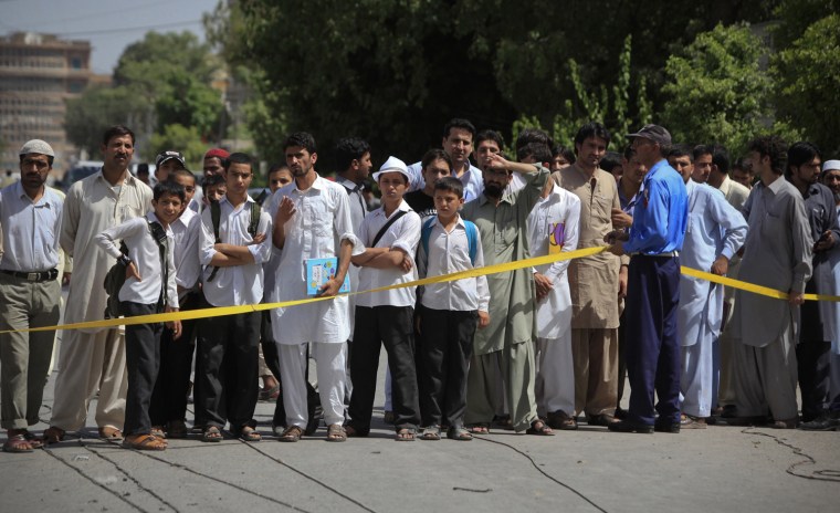 Image: School children and residents look on as a policeman cordons off the site of a bomb blast in Peshawar