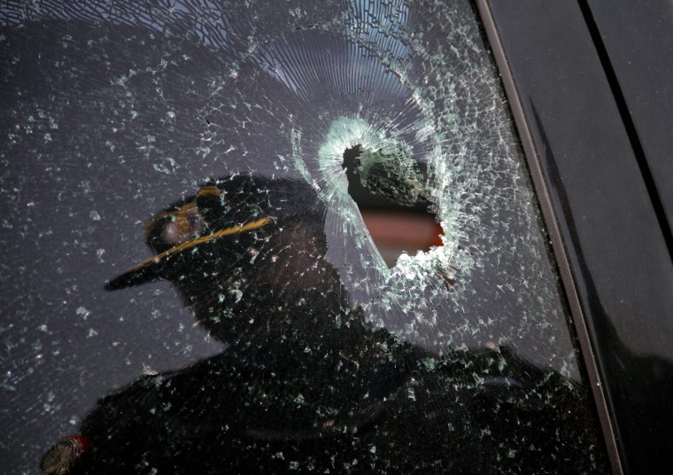 Image: A policeman is reflected in a window of a car shattered by bullets, currently parked in a police station in Karachi