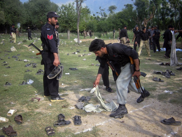 Image: Policemen pick-up the clothing and shoes of residents who were targeted by a suicide bomber during funeral prayers in Bero Shina, a town in Lower Dir District of Pakistan