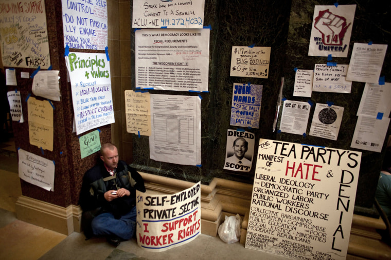Image: Man sits surrounded by protester signs on day eight of protests against budget cuts proposed by Wisconsin Governor Walker, at state Capitol in Madison
