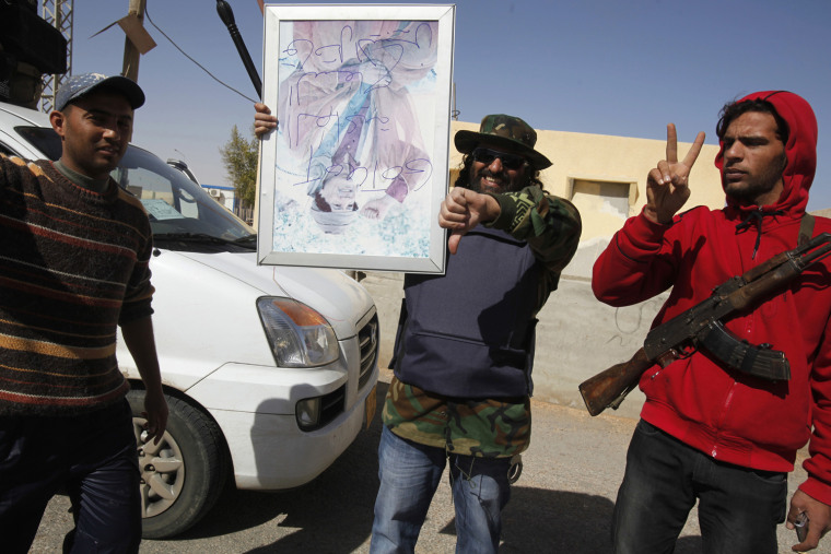 Image: Protesters hold a picture of Libyan leader Muammar Gaddafi upside-down in the Libyan-Egyptian border city of Masaed