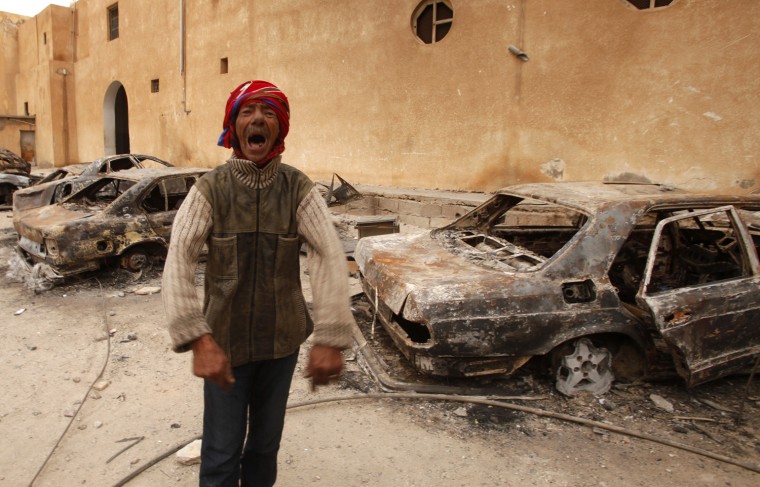 Image: A man gestures in front of burnt vehicles in a state security building in Tobruk, Libya