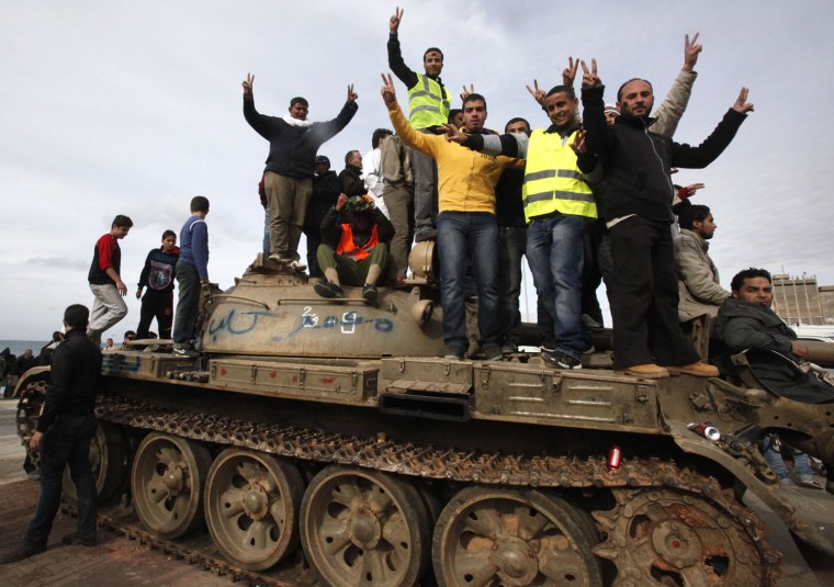 Image: Anti-government protesters make victory signs as they stand on an army tank near a square where people protest in Benghazi city
