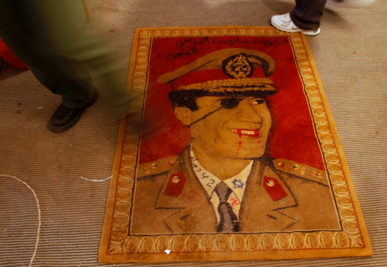 Image: A protester against Libyan leader Muammar Gaddafi walks over a rug depicting a defaced portrait of Gaddafi in Benghazi