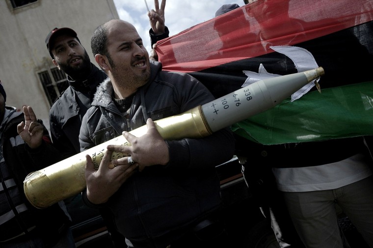 Image: A Libyan anti-government fighter carries a tank shell seized during clashes between anti-government protesters and Libyan government forces in the eastern city of Benghazi