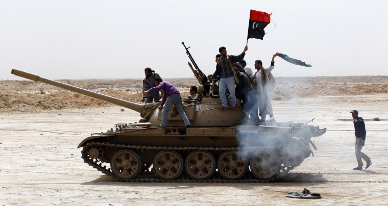 Image: Rebels wave a Kingdom of Libya flag as they ride on top of a tank on the outskirts of Ajdabiyah, on the road leading to Brega