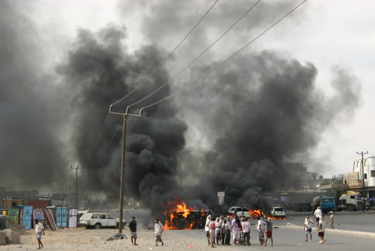 Image: Anti-government protesters look at a police vehicle which they had set ablaze during a protest demanding the ouster of Yemen's President Ali Abdullah Saleh