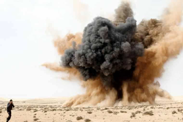 Image: A rebel holds his ears as a bomb launched by a Libyan air force jet loyal to Libya's leader Muammar Gaddafi explodes in the desert near Brega