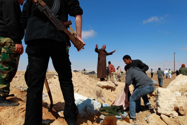 Image: Rebel fighters bury dead bodies killed by what the rebels say was a NATO airstrike, at the western gate of Ajdabiyah