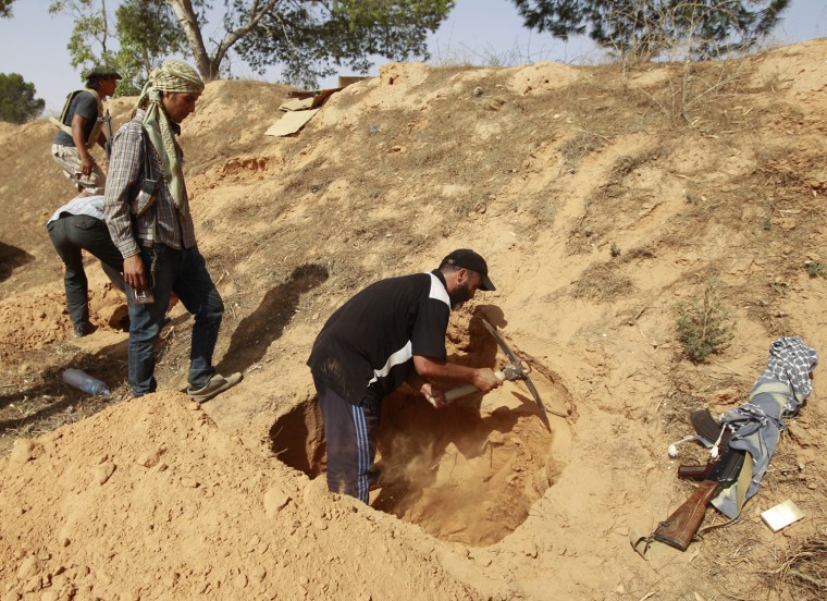 Image: Rebel fighter digs a hole to be used as a makeshift bunker on the outskirts of Zlitan near Misrata