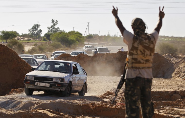 Image: A Libyan rebel fighter raises his arms as a convoy of residents flee fighting near the coastal town of Zawiyah