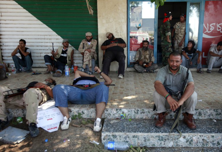 Image: Libyan rebel fighters rest in front of a shop as they advance through the town of Maia, 25 kms west of Tripoli