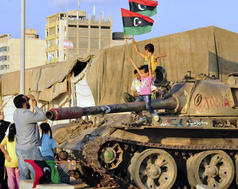Image: Libyan children sit on a tank while waving Kingdom of Libya flags near the court house in Benghazi