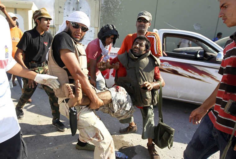 Image: Libyan rebel fighters carry an injured comrade near the gate of Bab al Aziziya  compound in Tripoli