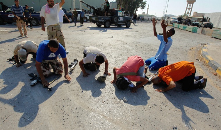 Image: Libyan rebel fighters pray at the enterance of Bab al-Aziziya compound in Tripoli