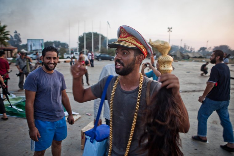 A rebel celebrates while wearing a hat, necklace and scepter thought to be taken from Gadhafi's Bab al-Aziziya compound, in Tripoli, Aug. 23, 2011.