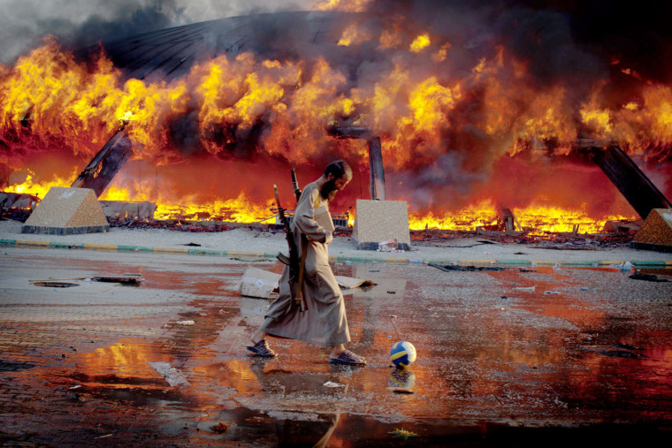 An armed rebel fighter kicks a soccer ball near Gadhafi's Bab al-Aziziya compound as it burns on Aug. 23, 2011. Libyan rebels captured the palace after days of fighting for control of Tripoli.