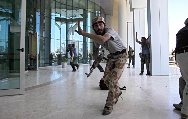 Rebel fighters and a television cameraman take shelter as an intense gun battle erupted outside the Corinthia hotel, where many foreign journalists were staying, in Tripoli, Aug. 25, 2011.  Libya's rebel leadership offered a $2 million bounty on Gadhafi's head, but the autocrat refused to surrender as his 42-year regime crumbles, fleeing to an unknown destination. Speaking to a local television channel, apparently by phone, Gadhafi vowed from hiding to fight on \"until victory or martyrdom.\"
