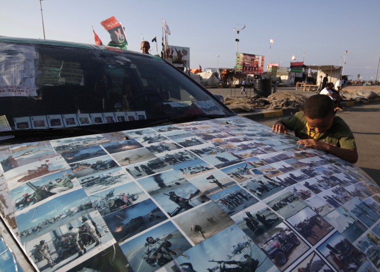 Image: A boy looks at photos of Libya's civil war stuck on the bonnet of a car in Tahrir Square in Benghazi
