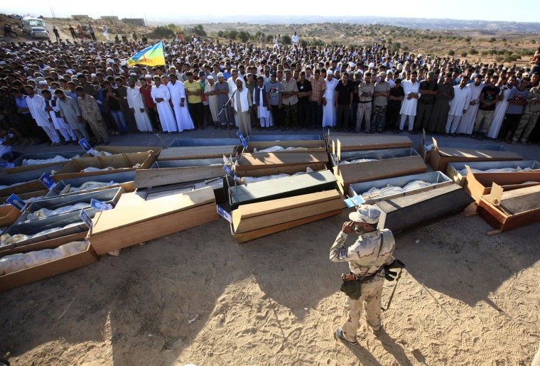 An rebel fighter stands near mourners during the funeral prayer for 35 people in the town of Al-Qalaa on Sept. 7, 2011. The bodies of the 35 people were found in a shipping container where, according to locals, the victims had been detained and tortured by security forces loyal Gadhafi.