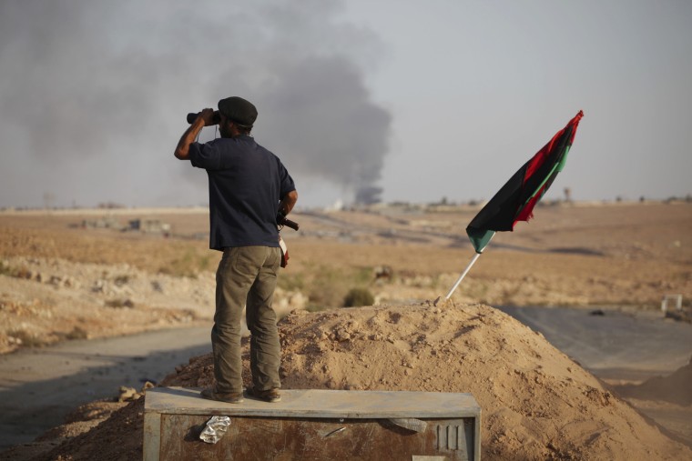 A former rebel fighter looks through binoculars at the northern gate of Bani Walid, as smoke rises from the town on Sept. 18, 2011