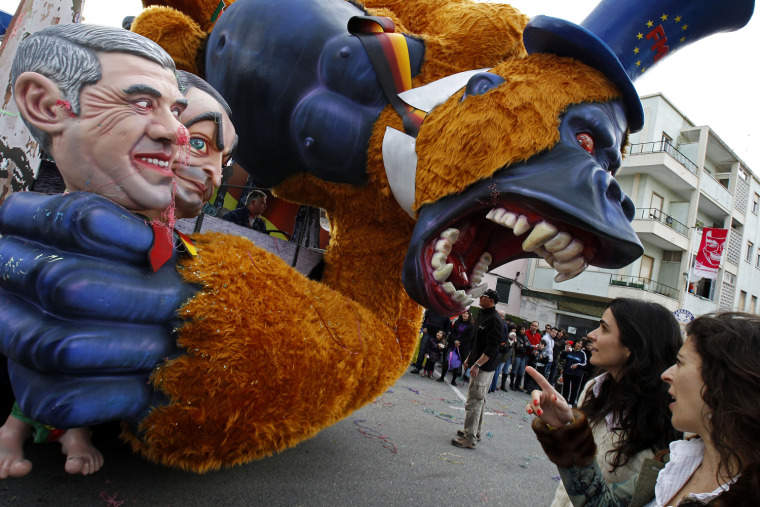 Image: Carnival revelers look at an IMF beast float during parade in Torres Vedras
