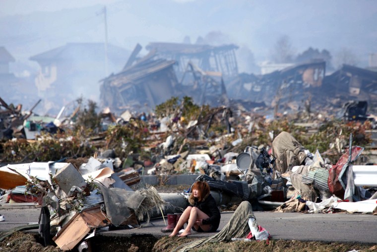 Image: A woman cries while sitting on a road amid the destroyed city of Natori, Miyagi Prefecture in northern Japan