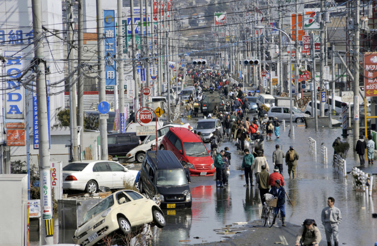 Image: People walk along a flooded street in Ishimaki City, Miyagi Prefecture in northern Japan