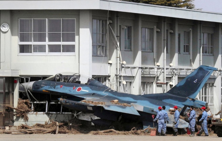 Image: Officers look at a Mitsubishi F-2 fighter aircraft of the Japanese Air Self-Defense Force which was swept by the tsunami into a building at Matsushima base in Higashimatsushima