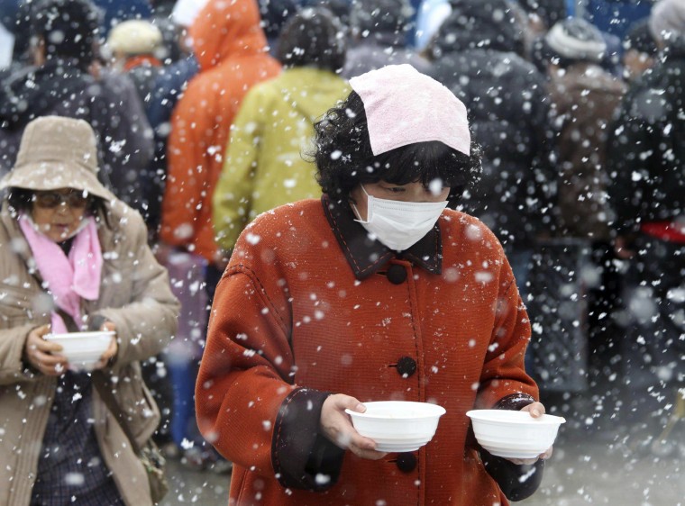 Image: Evacuees carry bowls of pork soup from a soup kitchen back to their makeshift shelter in Minamisanriku