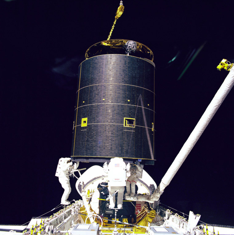 Mission Specialists Richard J. Hieb (from left), Thomas D. Akers, and Pierre J. Thuot hold onto the 4.5 ton International Telecommunications Organization Satellite (INTELSAT) VI after a six-handed \"capture\" was made minutes earlier on May 13, 1992, during the mission's third extravehicular activity. STS-49 was the maiden flight of the Space Shuttle Endeavour. The primary goal of its nine-day mission was to retrieve the Intelsat VI satellite, which failed to leave low earth orbit two years before, attach it to a new upper stage, and relaunch it to its intended geosynchronous orbit. After several attempts, the capture was completed with a three-person extra-vehicular activity, the first time that three people from the same spacecraft walked in space at the same time. It would also stand until STS-102 in 2001 as the longest EVA ever undertaken.