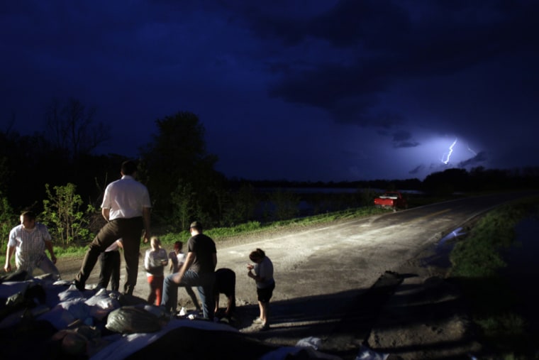 Image: Volunteers work to place sandbags atop a temporary levee to fight back floodwaters as lightning from a thunderstorm is seen in the background