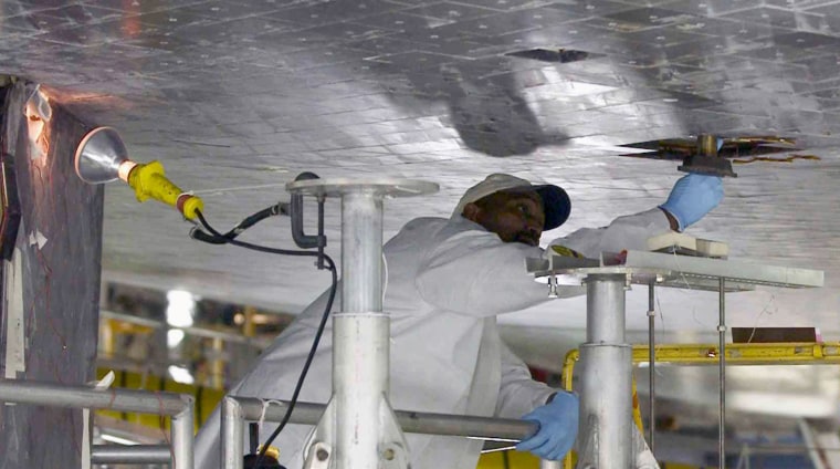 <HTML><META HTTP-EQUIV=\"content-type\" CONTENT=\"text/html;charset=utf-8\">
KENNEDY SPACE CENTER, FL - JANUARY 30: Izeal Battle, a worker from United Space 
Alliance, repairs heat-sheild tiles on the belly of Space Shuttle Atlantis in 
the Orbiter Processing Facility January 30, 2004 at Kennedy Space Center, 
Florida. Atlantis is the next shuttle scheduled for flight. (Photo by Matt 
Stroshane/Getty Images)