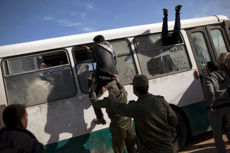 Image: Egyptians try to board a bus as a Tunisian Army soldier tries to stop one of them