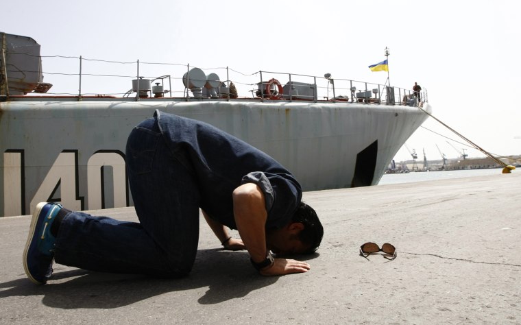 Image: A passenger kisses the ground and prays after disembarking from the Ukrainian Navy ship Konstantin Olshanskiy in Valletta's Grand Harbour