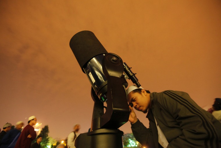 Image: A man uses a telescope as he tries to view the eclipse of the moon in Kuala Lumpur