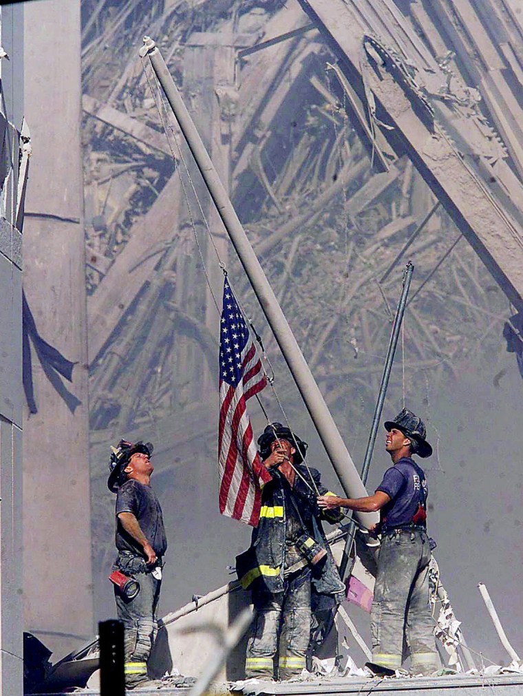 Firefighters raise a flag at the World Trade Center in New York  Tuesday, Sept. 11, 2001, as work at the site continues after hijackers crashed two airliners into the center. (AP Photo/The Record, Thomas E. Franklin)