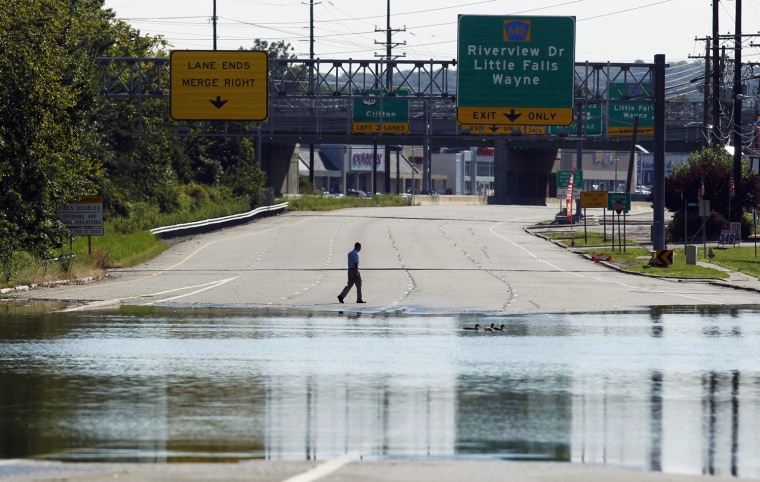 Image: A man walks across the road near a flooded section of Highway 23 in Wayne