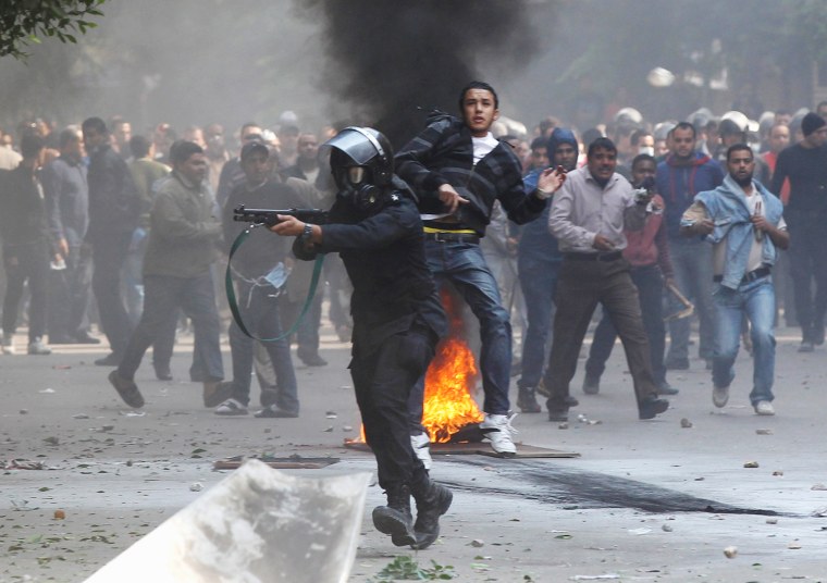 Image: A riot policeman aims a shotgun with rubber bullets at protesters, next to a plainclothes policeman during clashes in a side street near Tahrir Square in Cairo